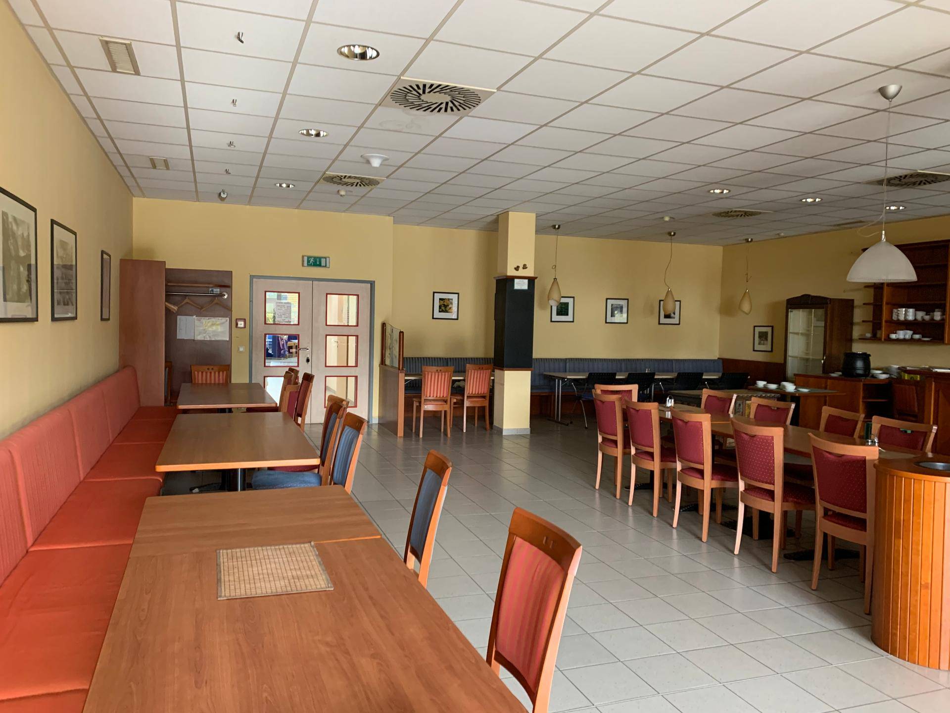 Weitläufiger Speisesaal mit verschiedenen Sitzbereichen, Holztischen und Fliesenboden, ideal für größere Gruppen.