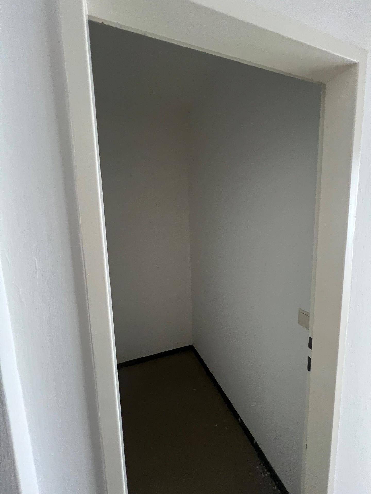 Kleiner, leerer Abstellraum mit weißen Wänden und dunklem Boden, ideal für zusätzlichen Stauraum.