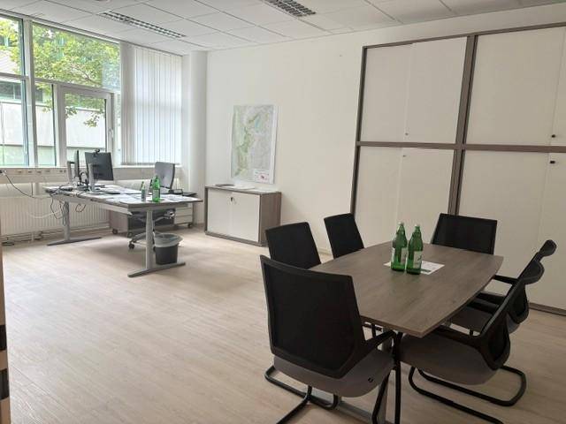 Geräumiges Büro mit mehreren Arbeitsplätzen und einem großen Besprechungstisch, viel Tageslicht.
