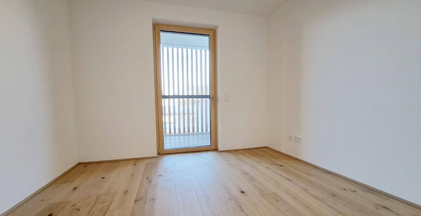 Helles Zimmer mit Holzboden und Zugang zu einem Balkon, ideal als Schlaf- oder Arbeitszimmer.