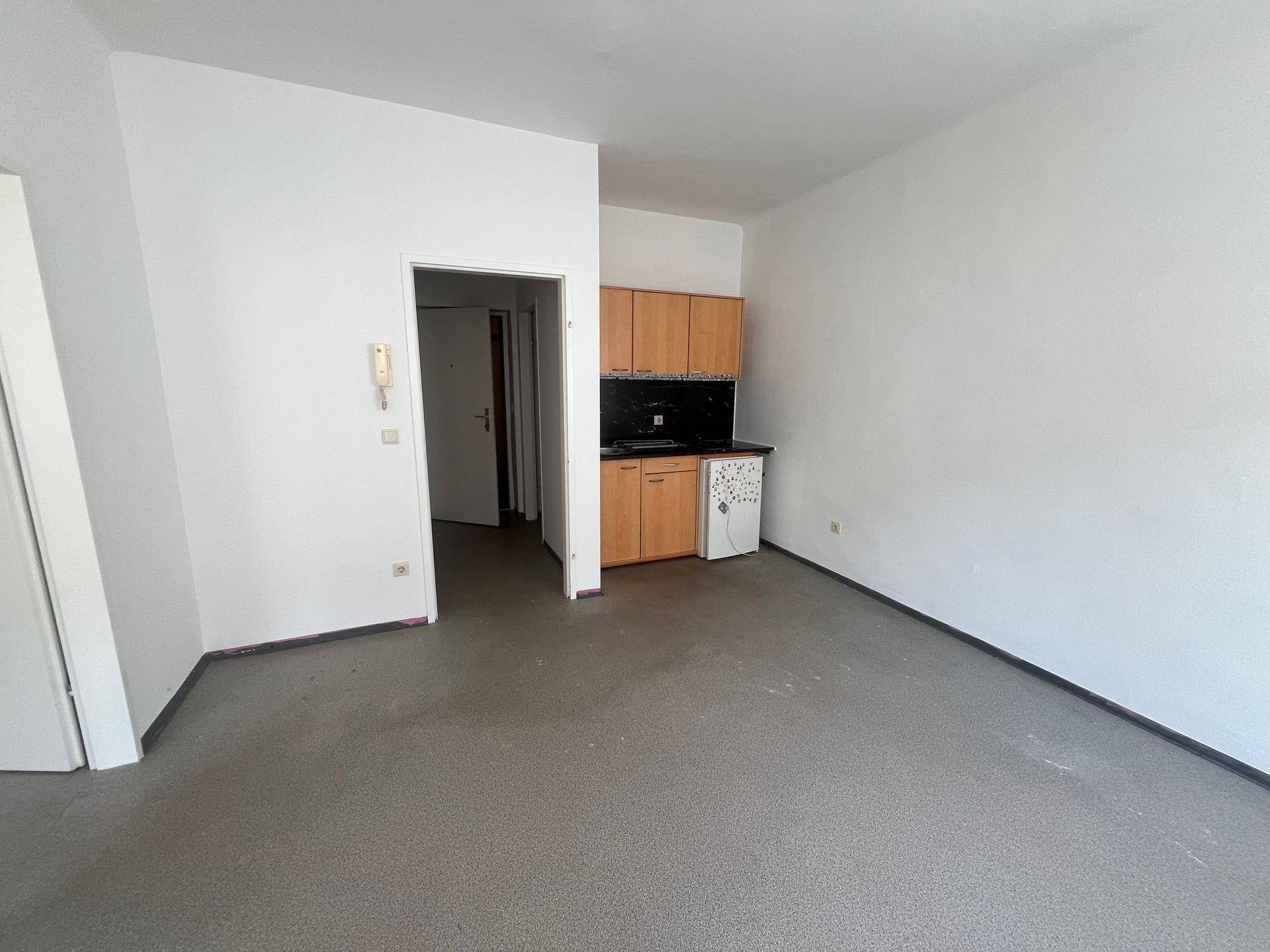 Wohnbereich mit integrierter kleiner Küchenzeile, weißen Wänden und dunklem Boden, ideal für ein Studio-Apartment.