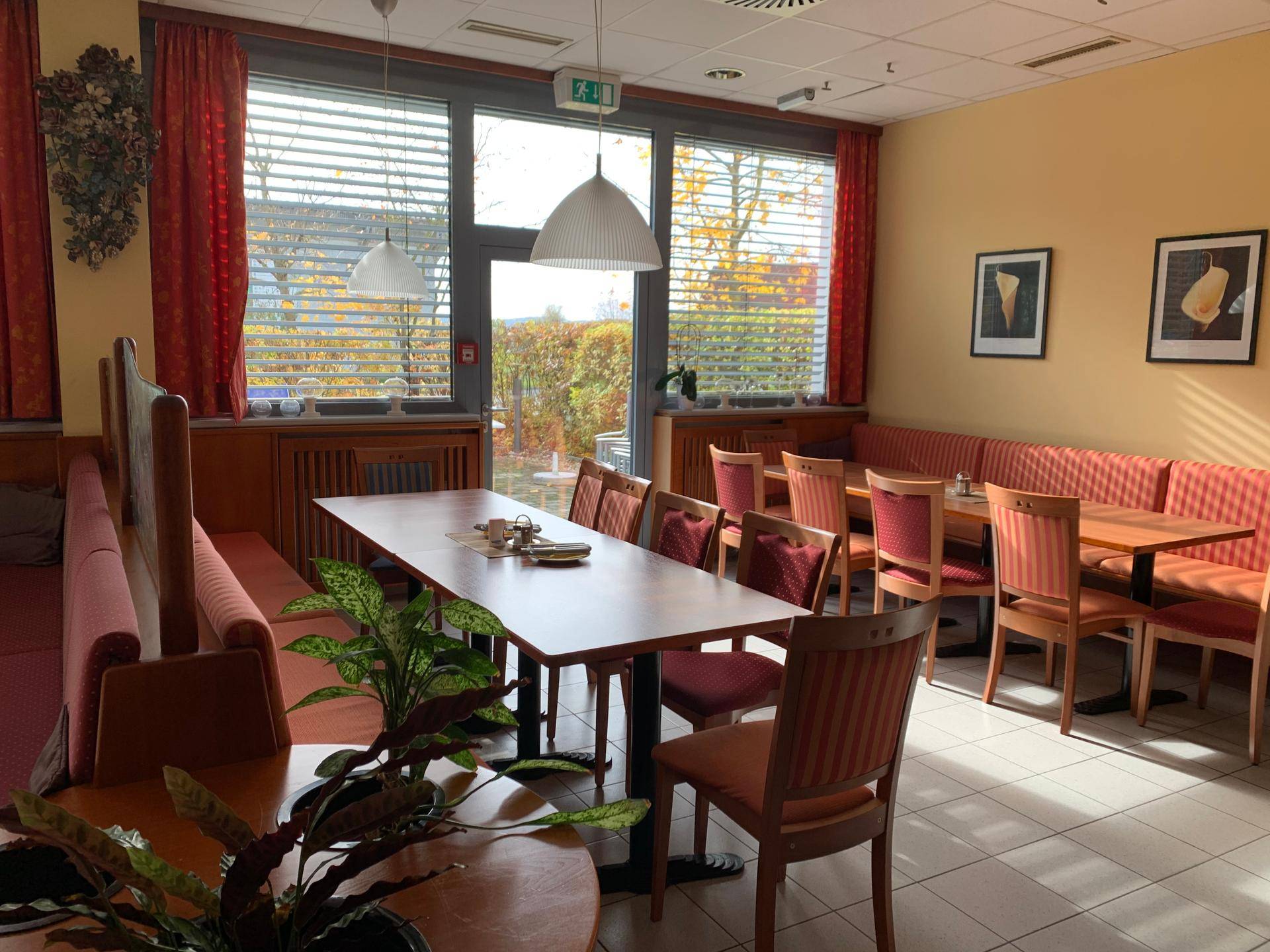 Gemütlicher Bereich im Speisesaal mit langer Tafel, Sitzbänken und großen Fenstern mit Blick ins Grüne.