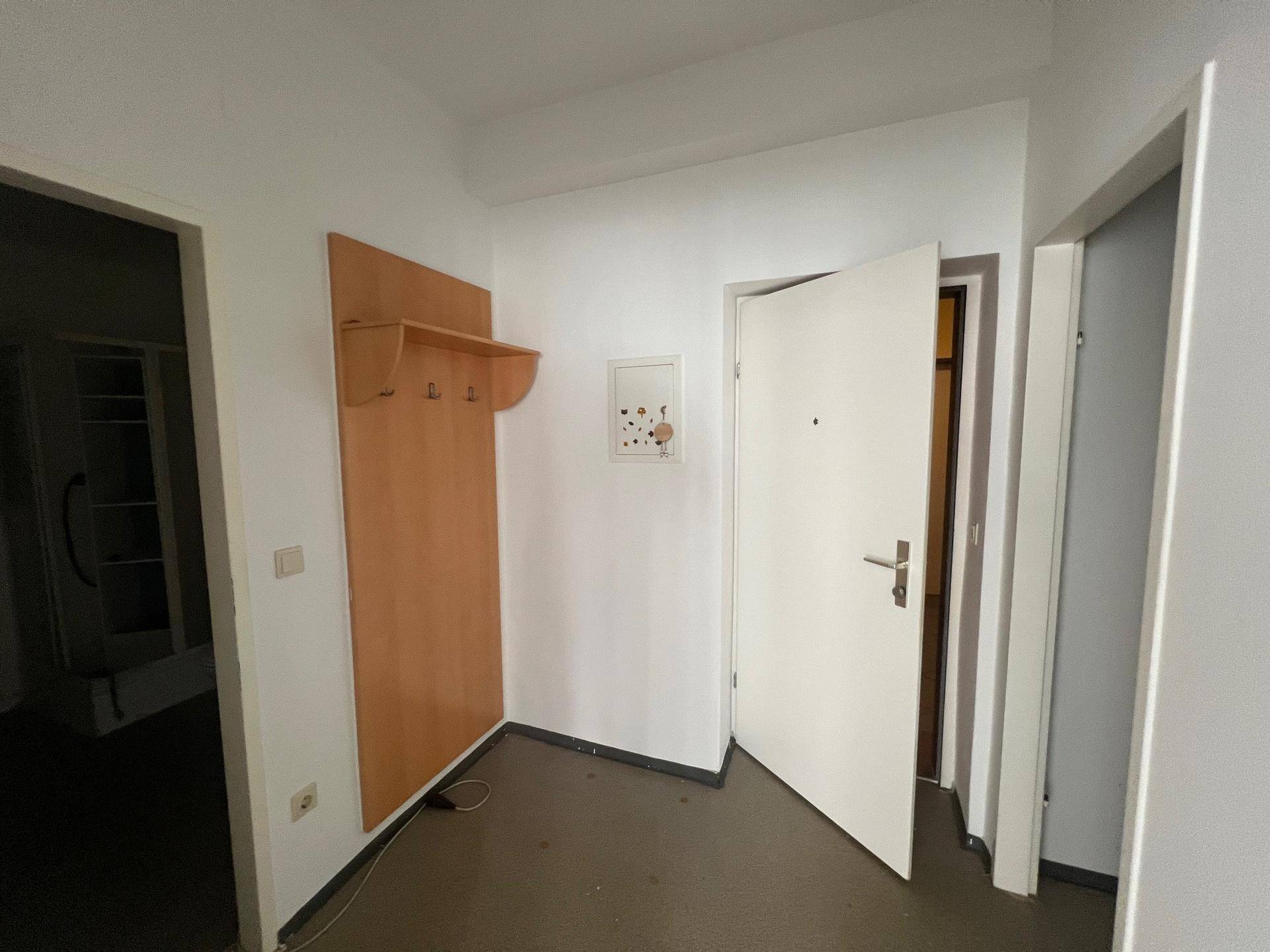 Eingangsbereich mit einer schlichten Garderobe aus Holz und dunklem Boden, der zu weiteren Räumen führt.