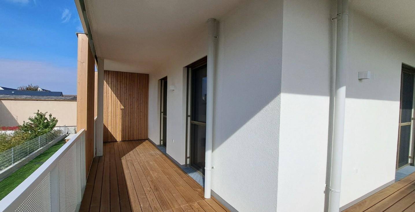 Langer Balkon mit Holzdielen und weißem Geländer, ideal für entspannte Stunden im Freien.