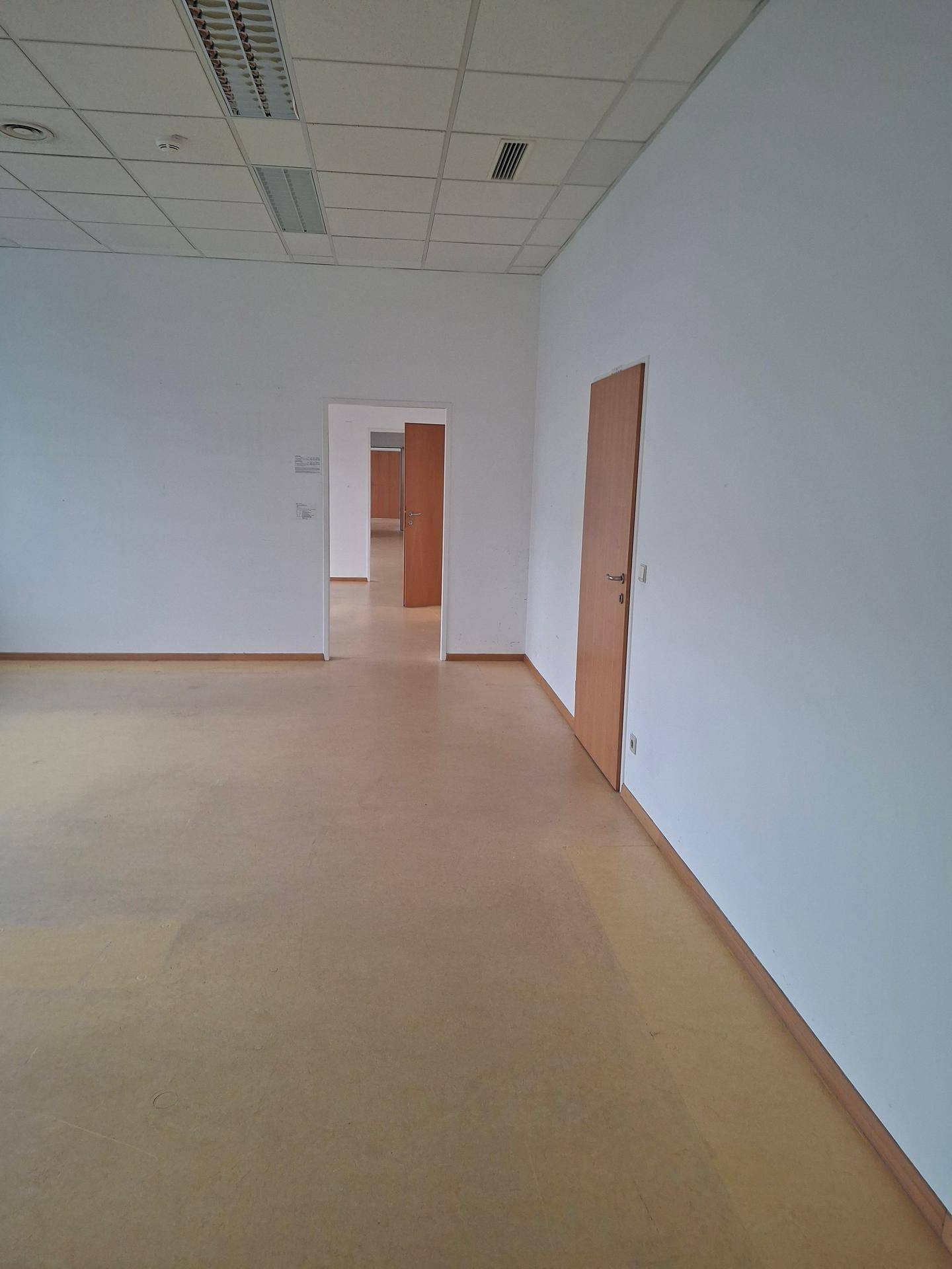 Geräumiger, leerer Bürobereich mit hellem Laminatboden und Blick in einen langen Flur.