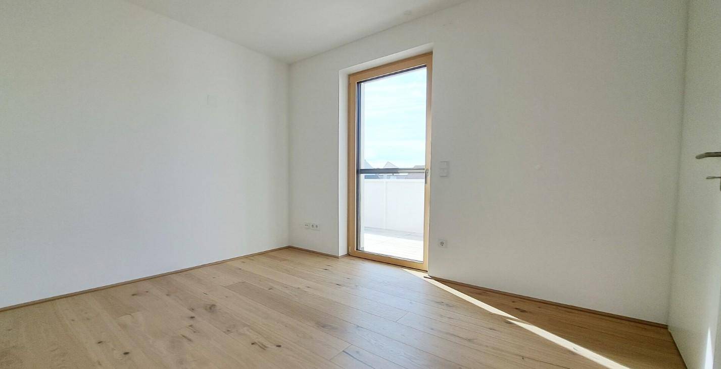Helles Schlafzimmer mit Holzboden und Zugang zu einem kleinen Balkon, bietet viel Tageslicht.