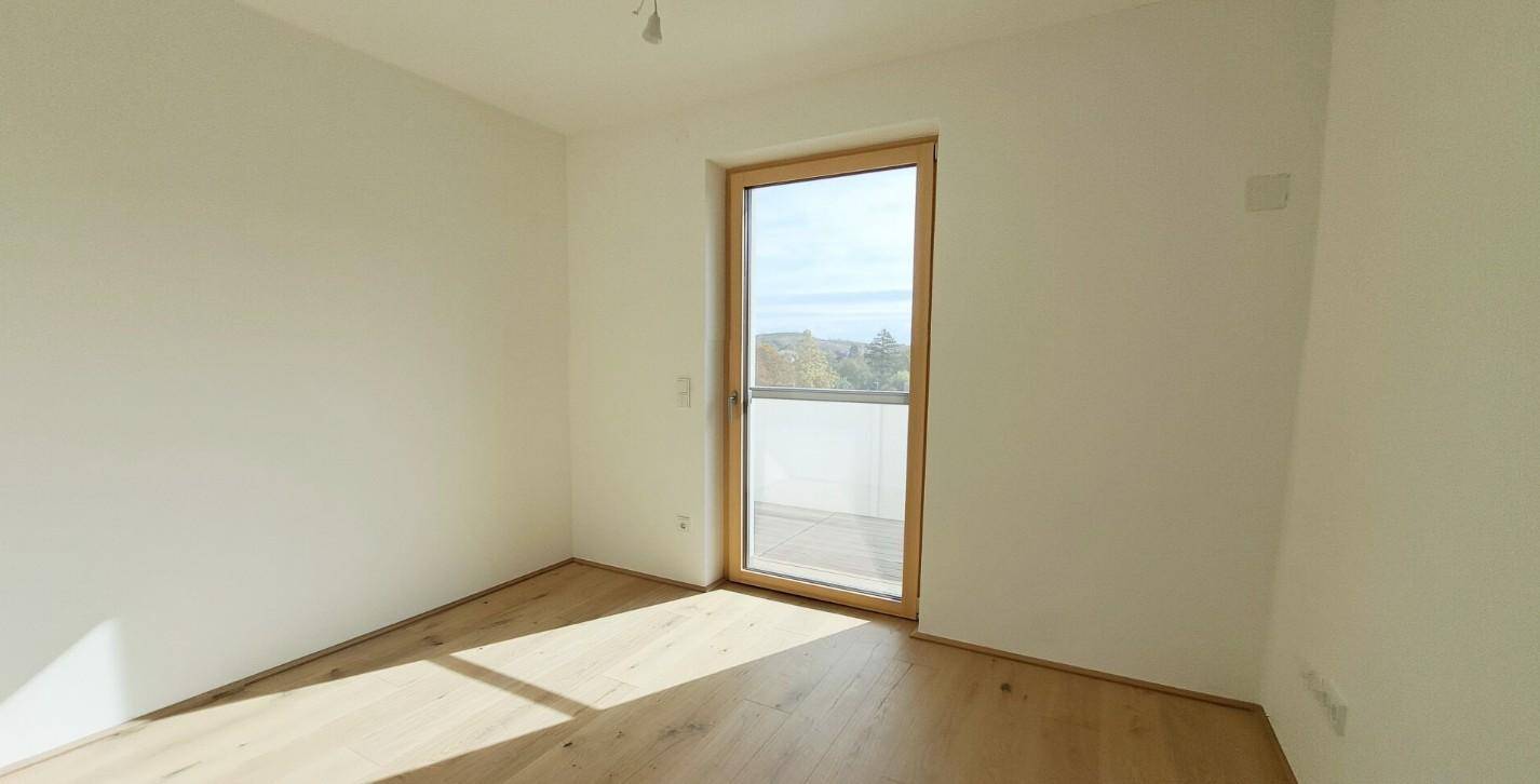 Geräumiges Schlafzimmer mit Holzboden und Balkonzugang, bietet eine helle und freundliche Atmosphäre.