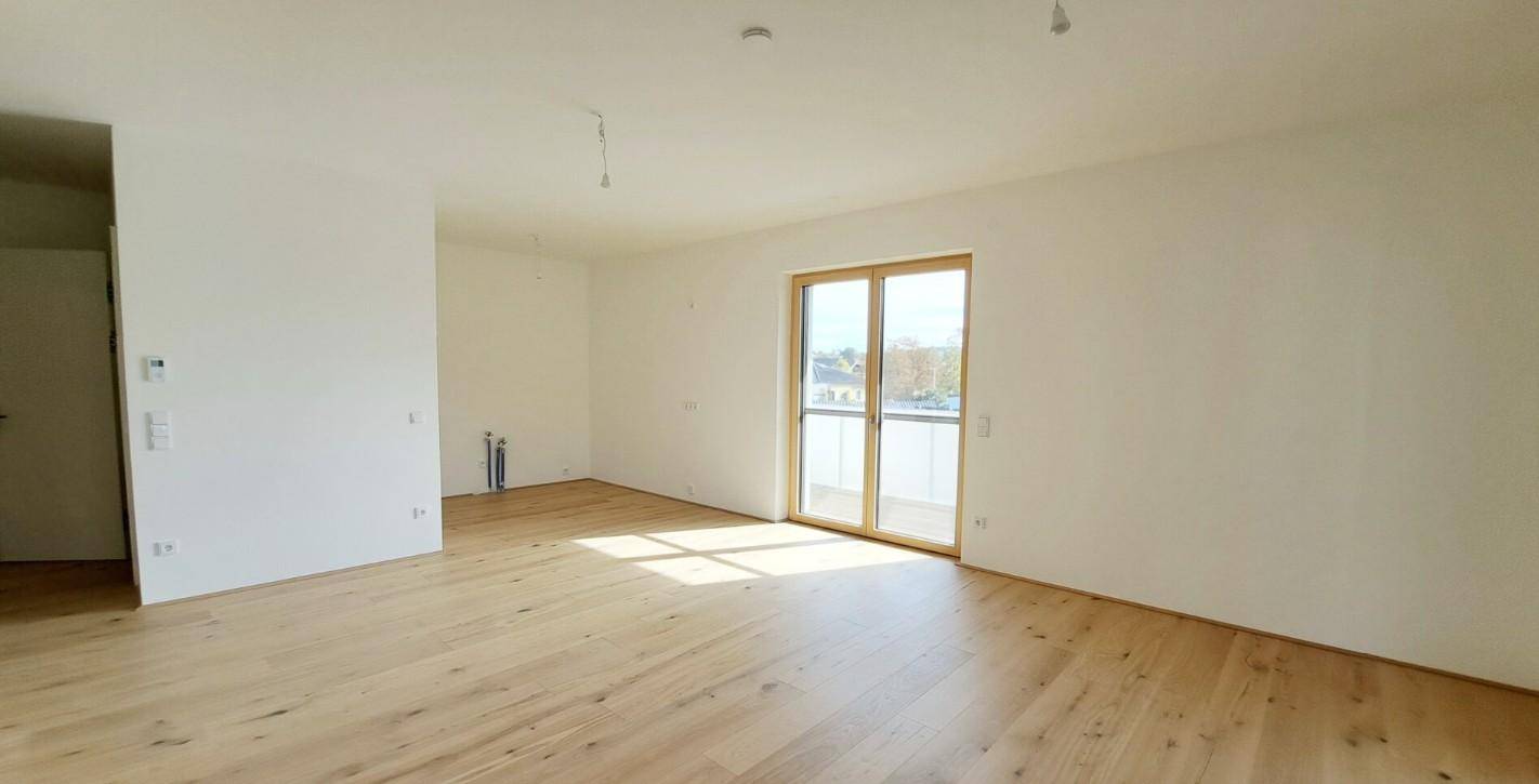Großer, heller Raum mit Holzboden und Balkonzugang, bereit zur individuellen Gestaltung und Nutzung.