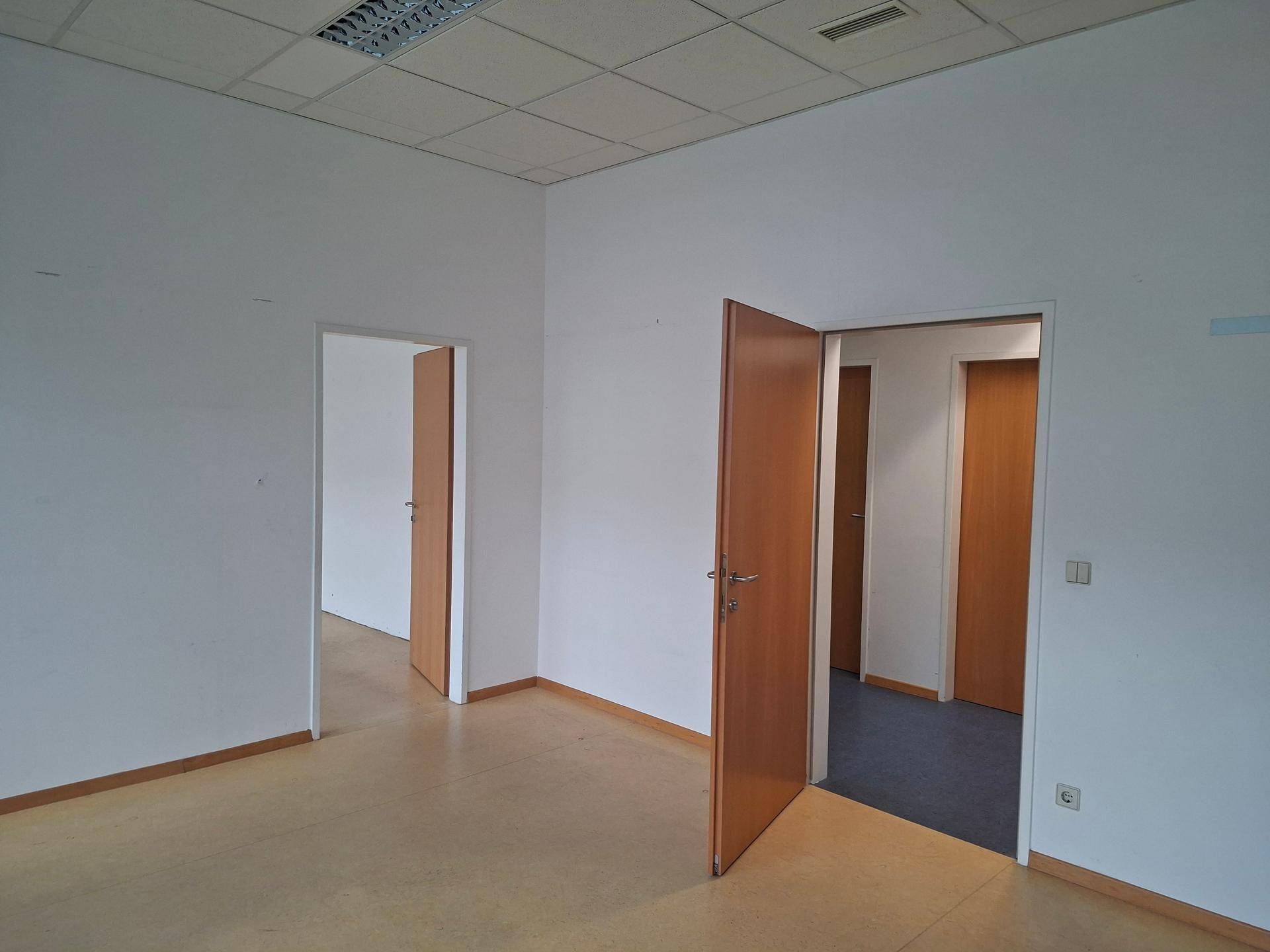 Leerer Büroraum mit mehreren Türen, die zu angrenzenden Bereichen führen, und hellem Boden.