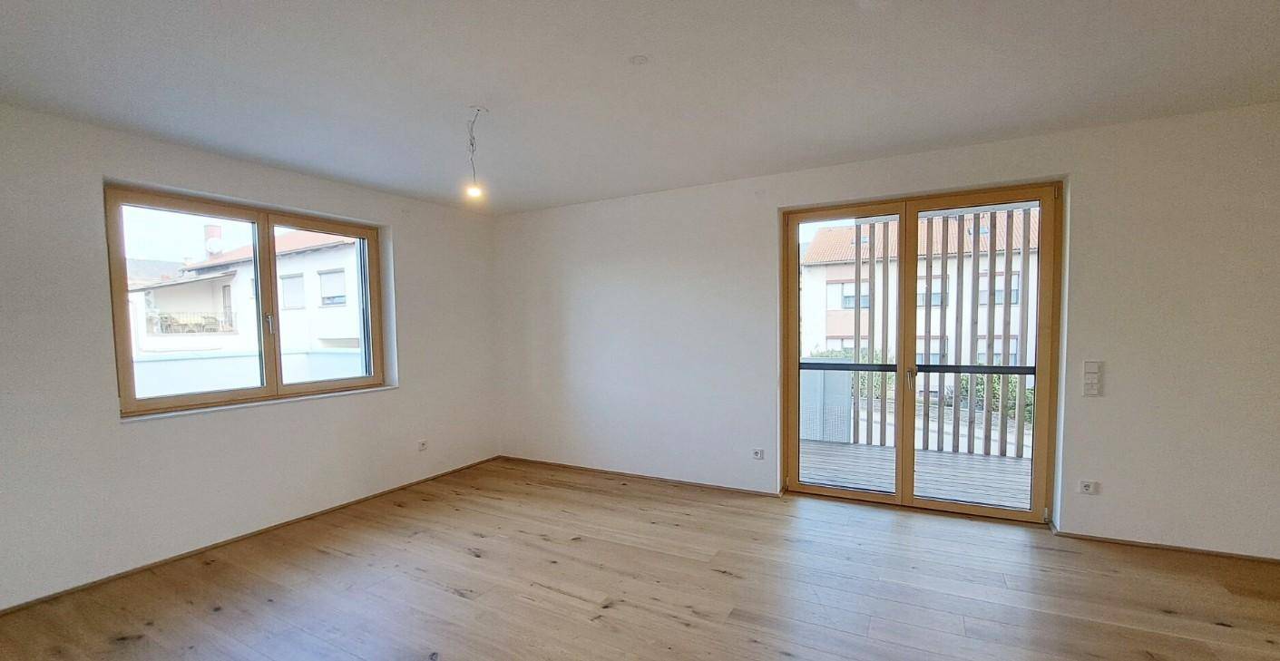 Großer, heller Raum mit Holzboden, zwei Fenstern und einer Balkontür, ideal für Wohnzwecke.