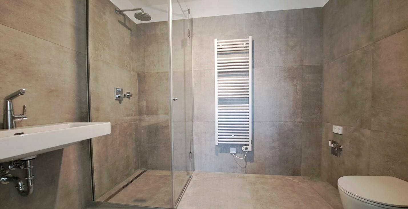 Modernes Badezimmer mit begehbarer Dusche, grauen Fliesen und beheiztem Handtuchhalter für Komfort.