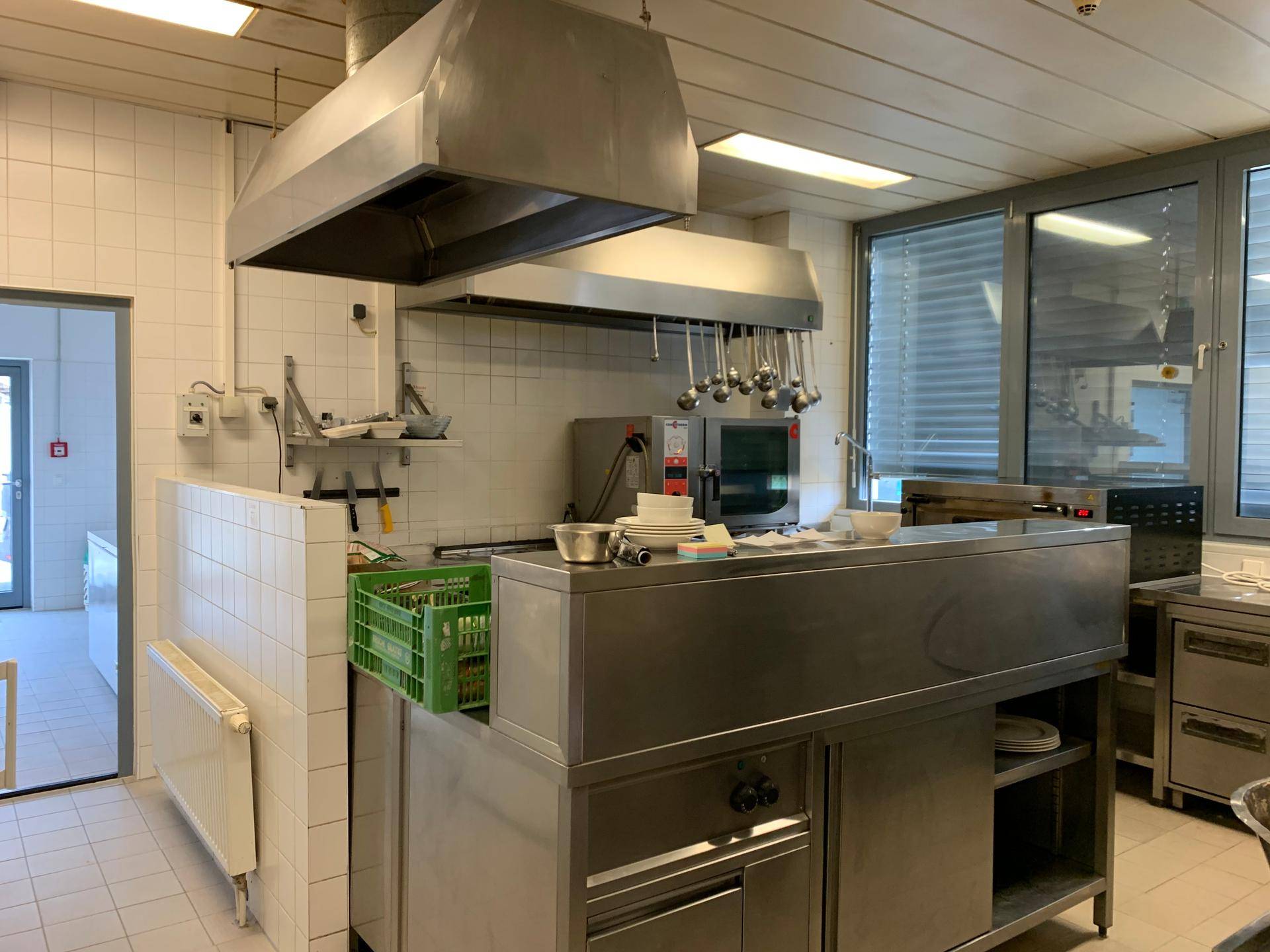 Gut ausgestattete Gewerbeküche mit großer Dunstabzugshaube, Edelstahloberflächen und funktionaler Einrichtung.