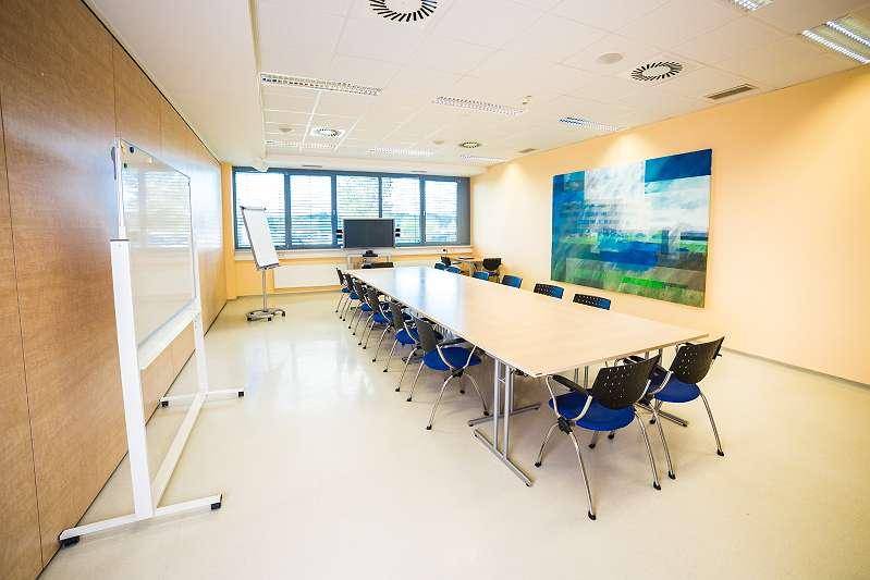 Großer Konferenzraum mit langem Tisch, vielen Stühlen und einem Fenster mit Jalousien für Besprechungen.