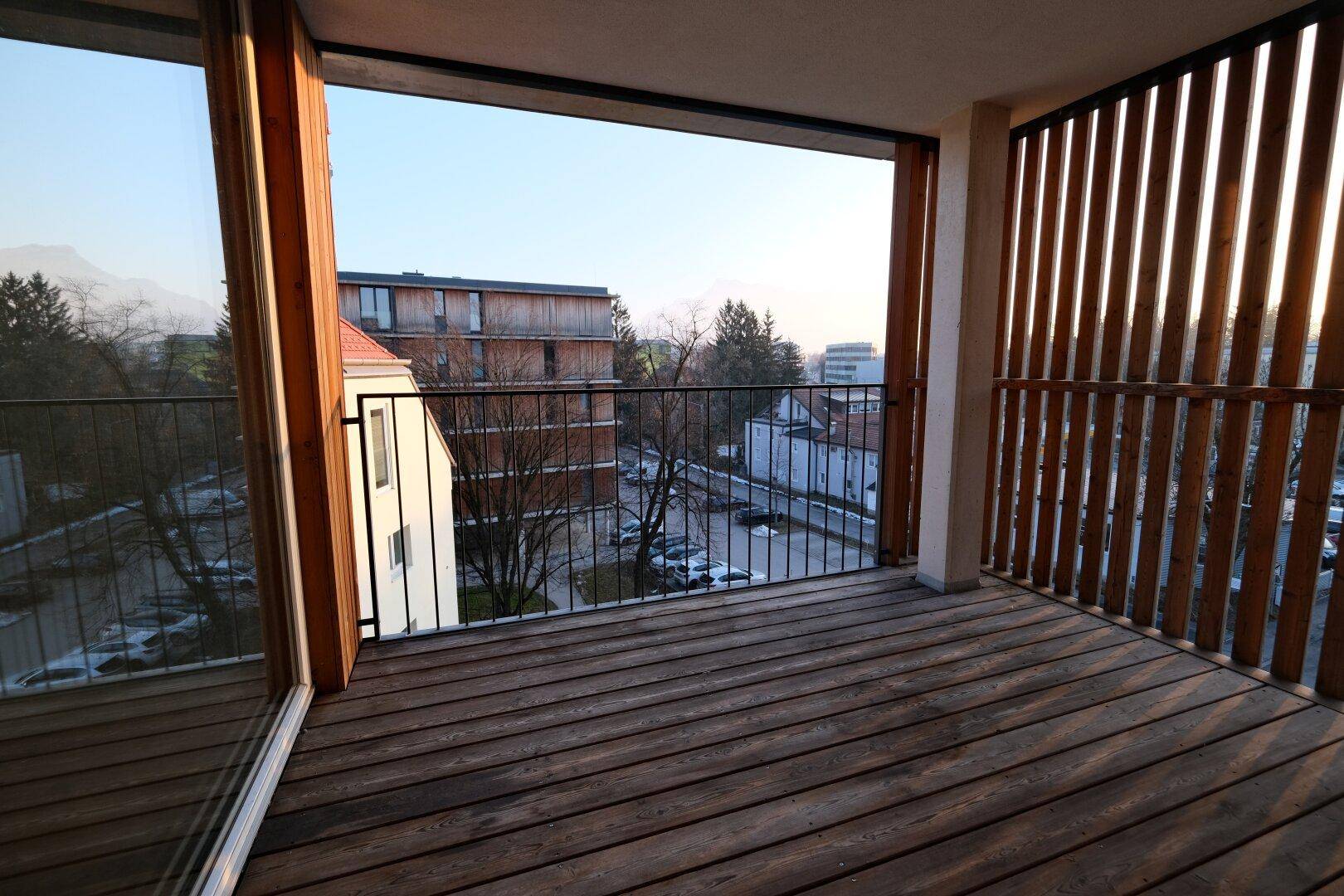 Geräumiger Balkon mit Holzboden und vertikalen Holzlamellen für Privatsphäre und Ausblick.
