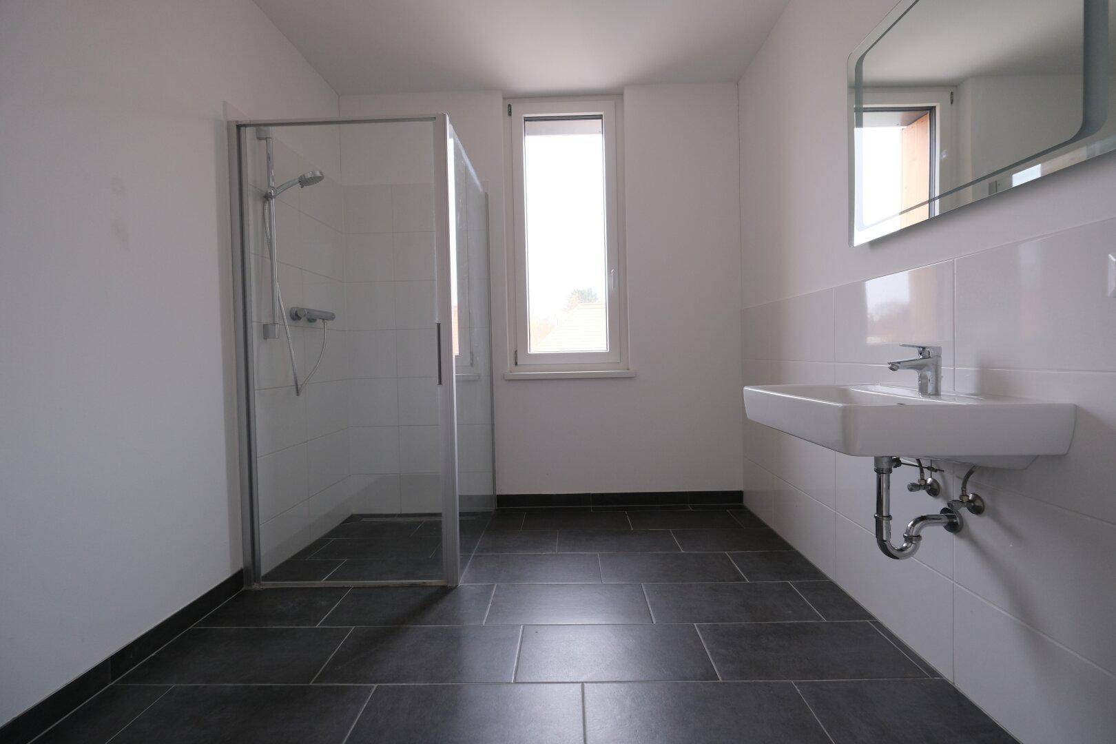 Modernes Badezimmer mit ebenerdiger Dusche, großem Waschbecken und Fenster für Tageslicht.