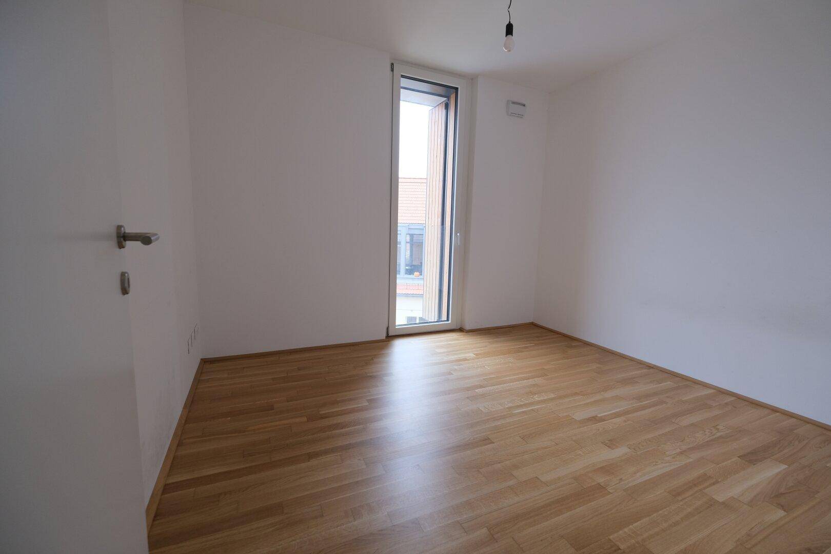 Helles Schlafzimmer mit Holzboden und Zugang zu einem Außenbereich durch eine große Tür.