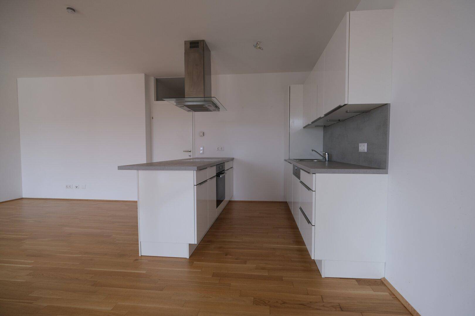 Moderne Einbauküche mit weißen Schränken, Kücheninsel und Dunstabzugshaube in offenem Wohnbereich.