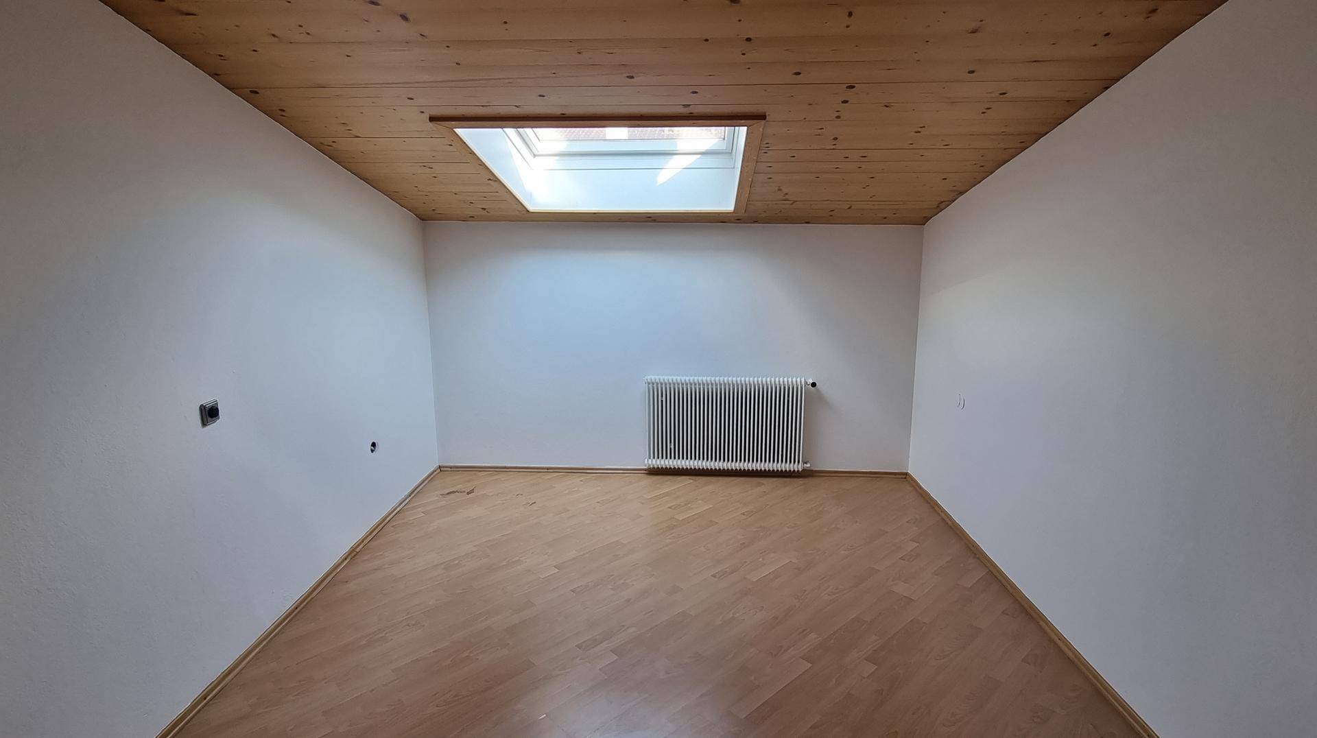 Zimmer mit Holzdecke, Parkettboden und Dachfenster für viel natürliches Licht.