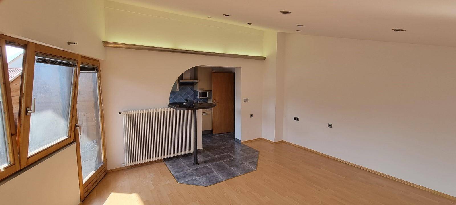 Offener Wohnbereich mit Holzboden, Heizkörper und Blick auf den Balkon durch große Fenster.