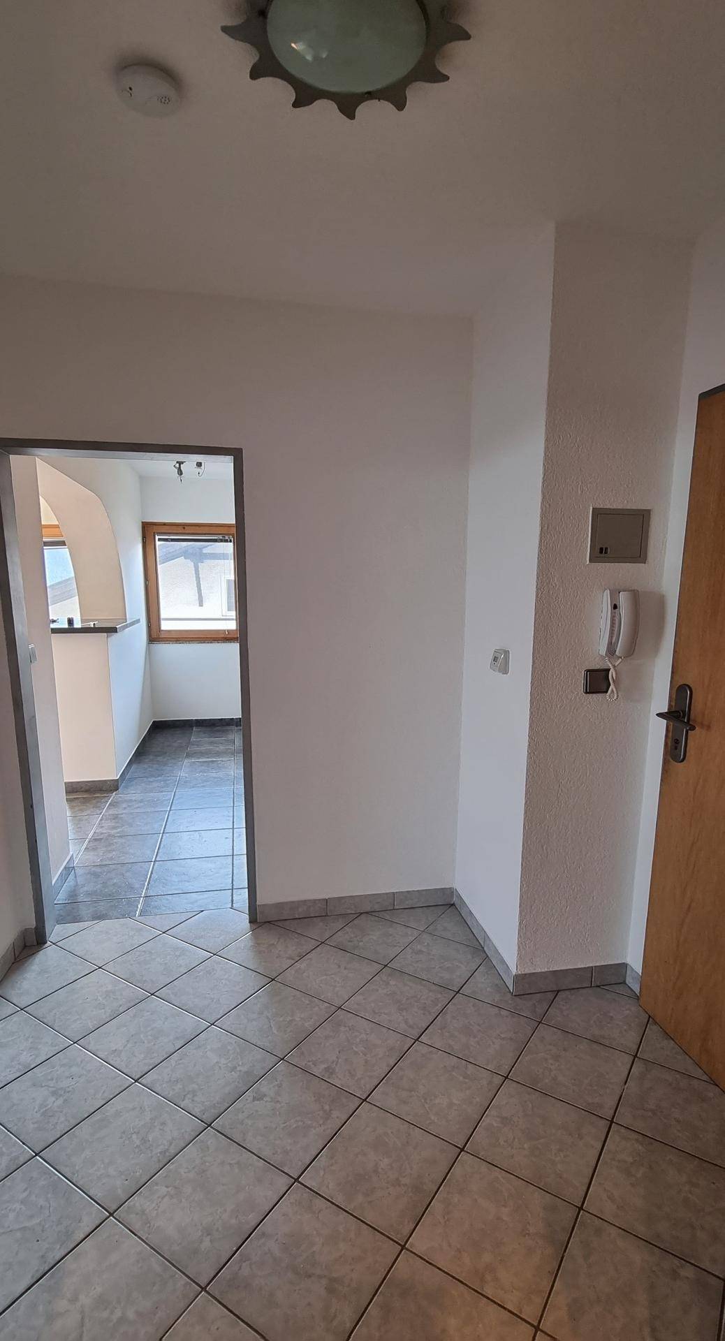 Eingangsbereich mit Fliesenboden, Gegensprechanlage und Blick in den Wohnbereich.