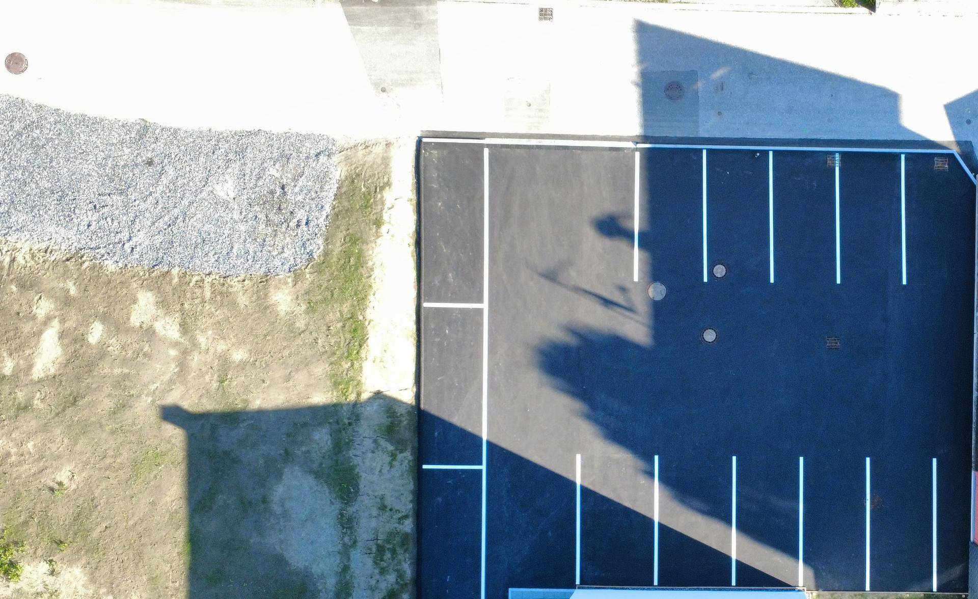 Luftaufnahme eines neu angelegten Parkplatzes mit frischen Markierungen und angrenzenden Flächen.