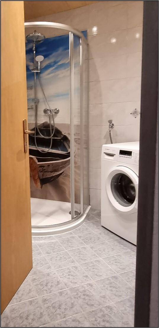 Modernes Badezimmer mit Duschkabine und Waschmaschine auf Fliesenboden.