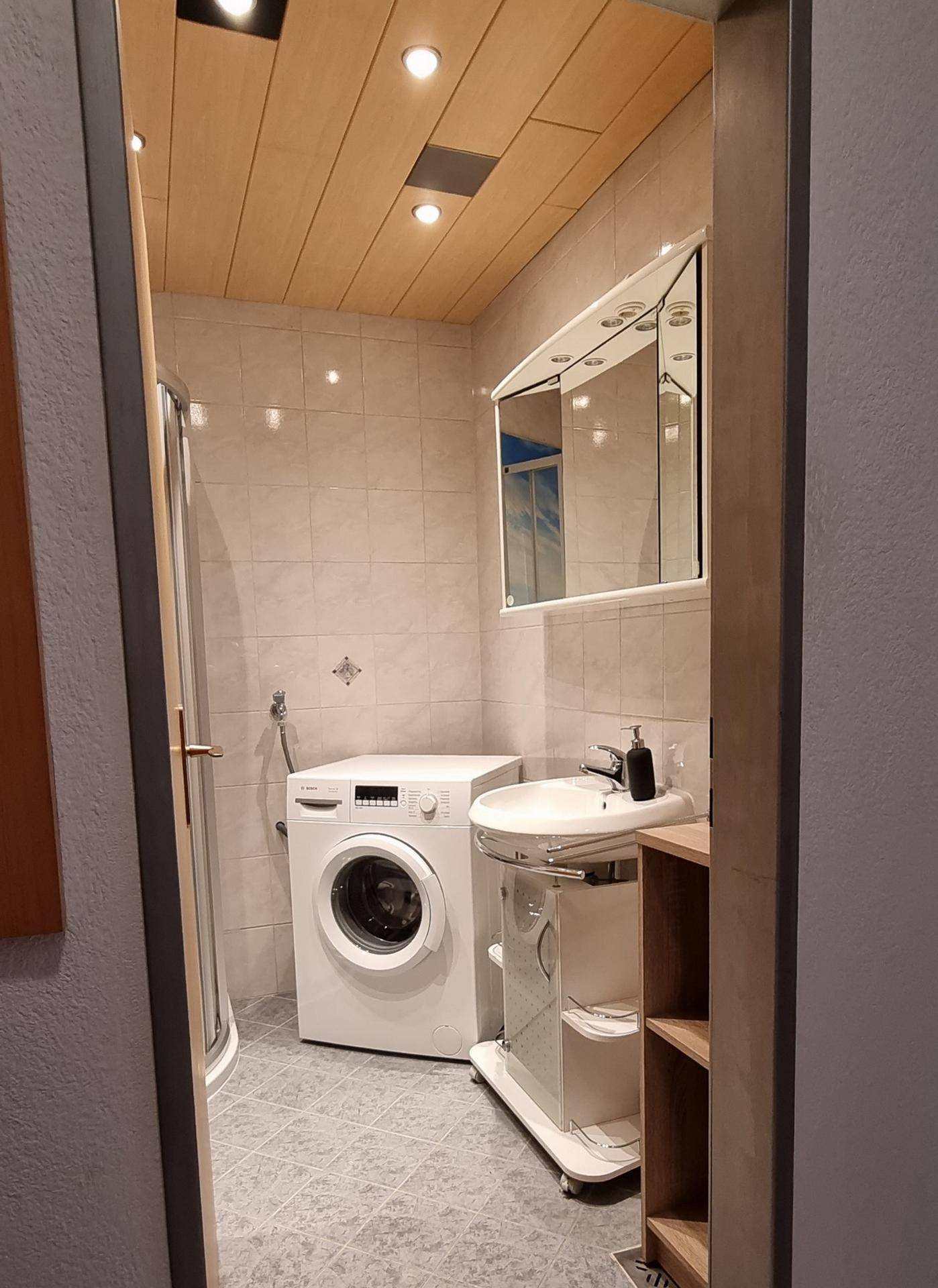 Badezimmer mit Holzdecke, Waschbecken, Spiegelschrank und Waschmaschine.