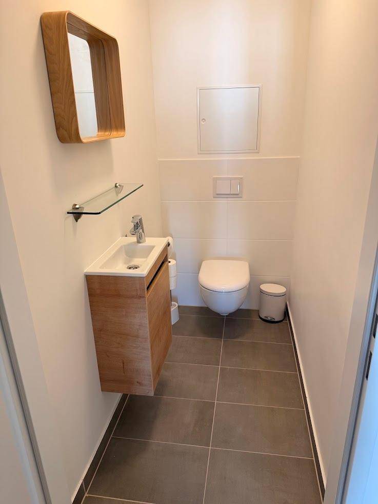 Modernes Gäste-WC mit wandhängendem WC, kleinem Waschbecken und Holzspiegel.