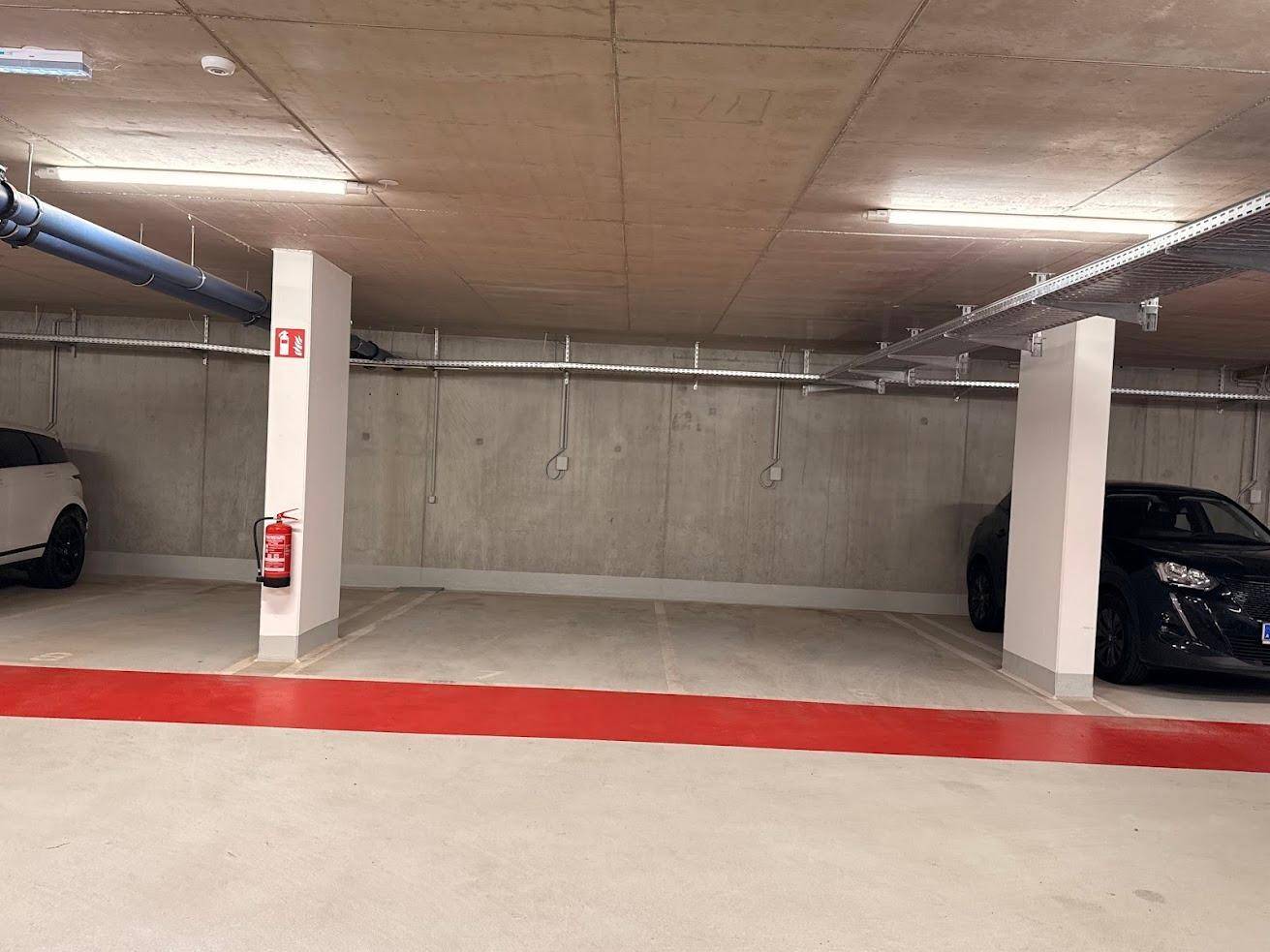 Tiefgarage mit Betonwänden, sichtbaren Installationen und markierten Parkplätzen.
