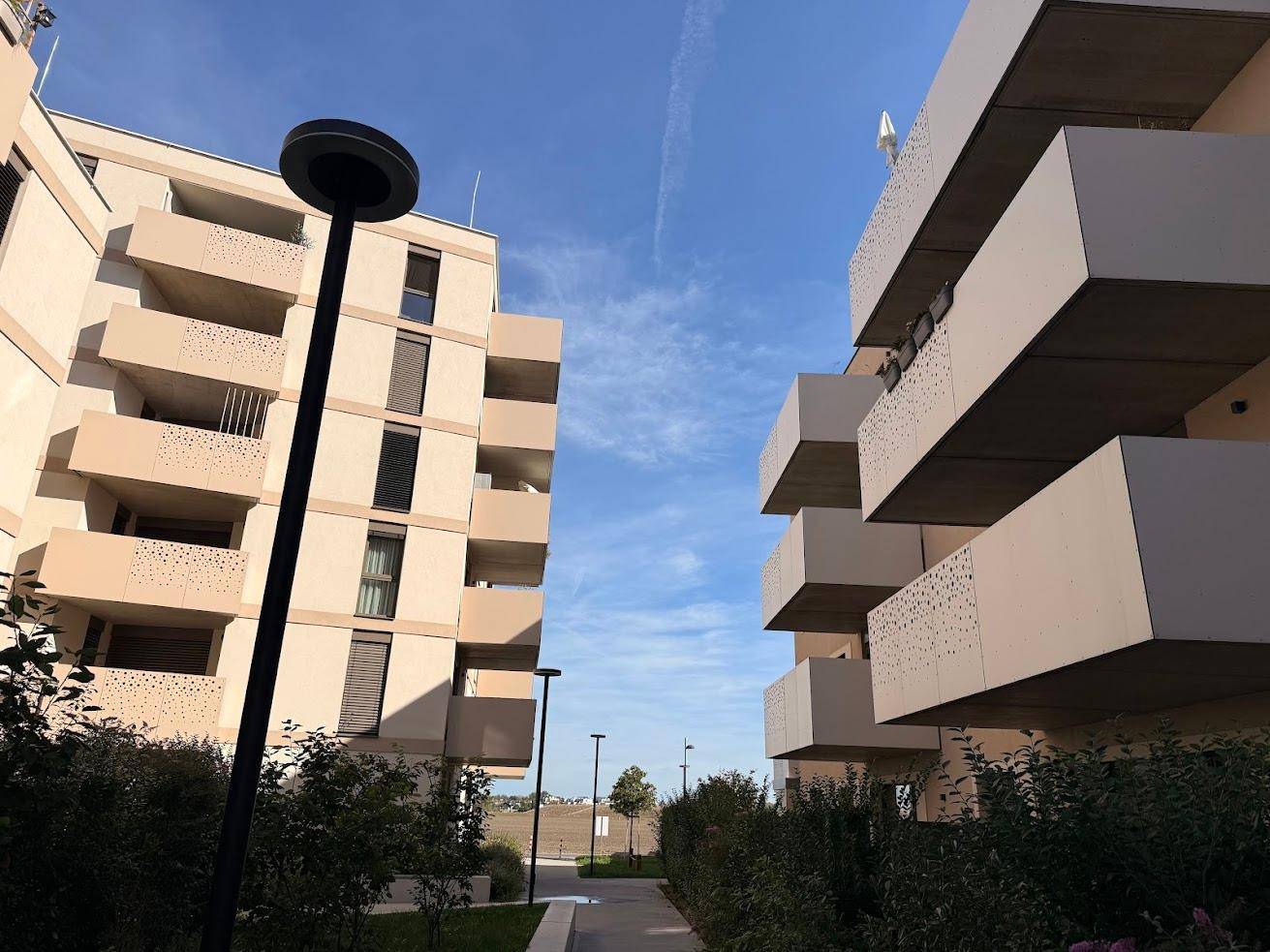 Gehweg zwischen zwei modernen Wohngebäuden mit Balkonen und gepflegten Grünflächen.