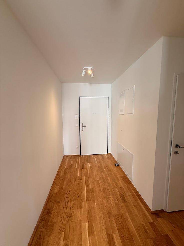 Heller Flur einer Wohnung mit Eichenparkettboden und weiß gestrichenen Wänden.