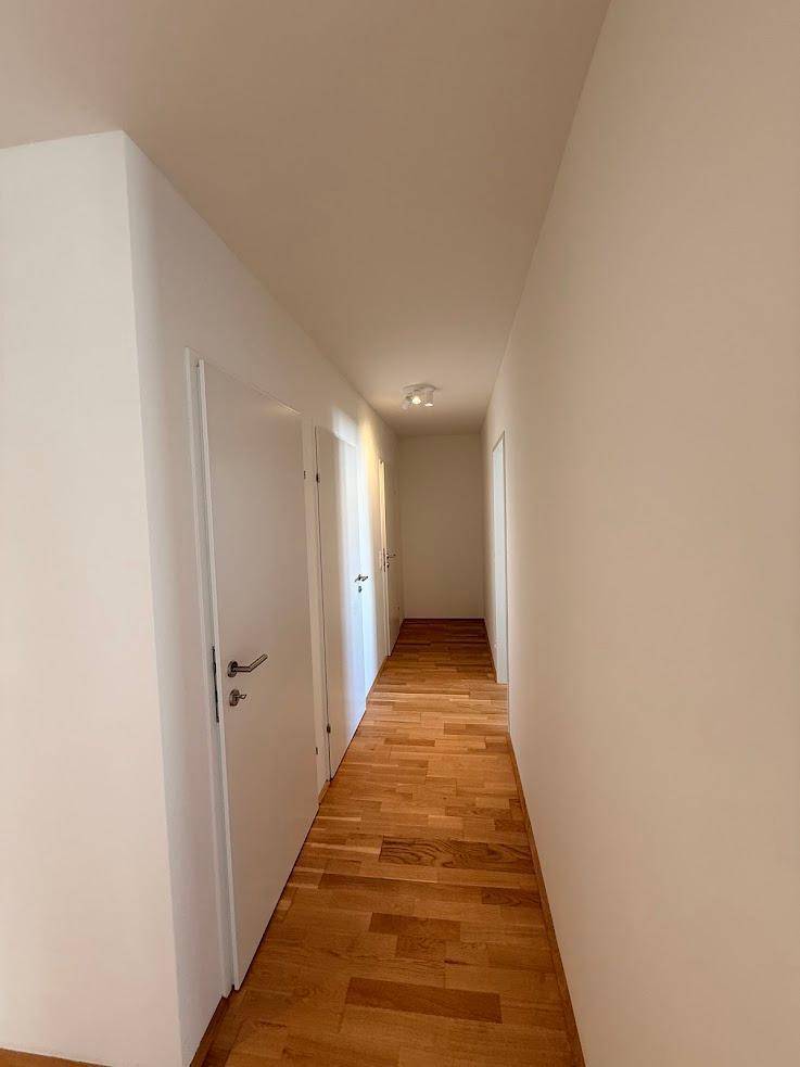 Langer, heller Flur einer Wohnung mit Holzboden und mehreren weißen Türen.