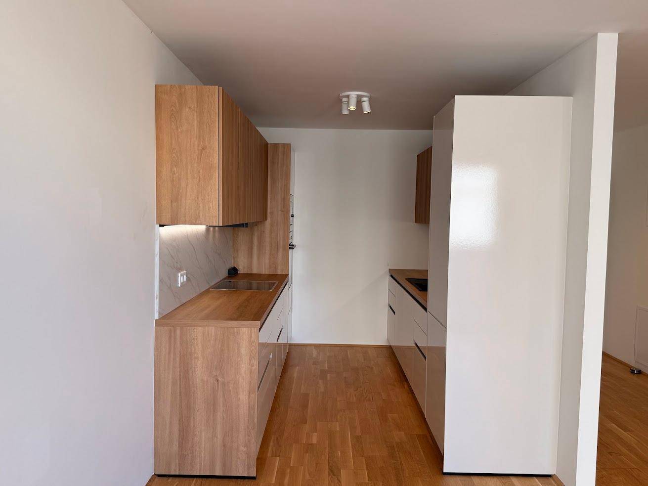 Moderne Küchenzeile mit Holzschränken, weißen Fronten und integrierten Geräten.