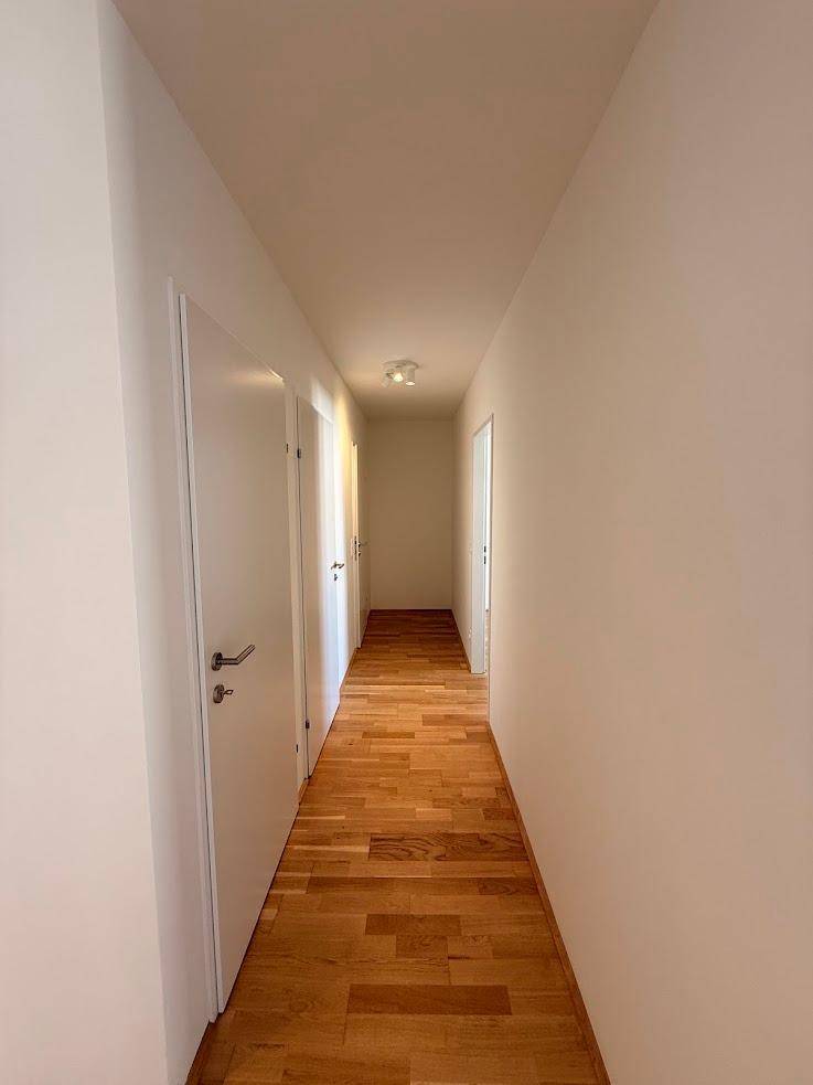 Langer, heller Flur mit Holzboden und weißen Wänden, der eine klare Raumaufteilung bietet.