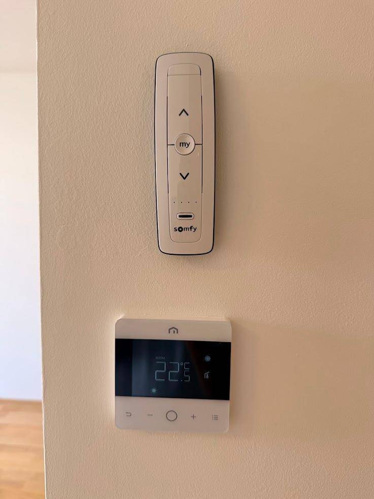 Wandmontierte Steuerung für Jalousien und Raumtemperatur in einer modernen Wohnung.
