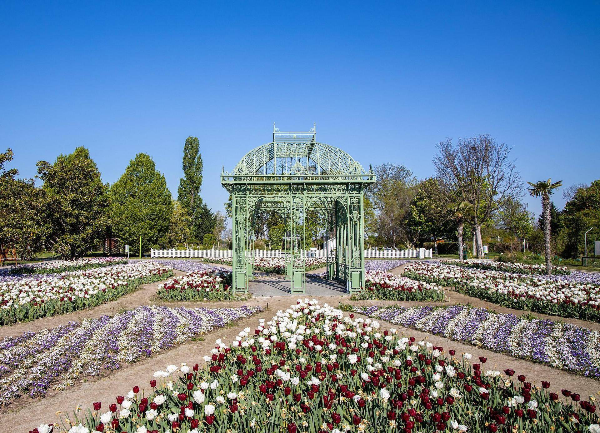 Wunderschöner Garten mit bunten Blumenbeeten, einem eleganten Pavillon und klarem blauen Himmel.
