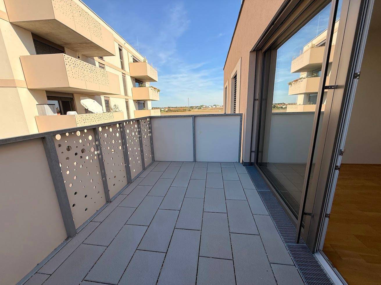 Heller Balkon mit Fliesenboden und perforiertem Geländer, ideal für Entspannung im Freien.