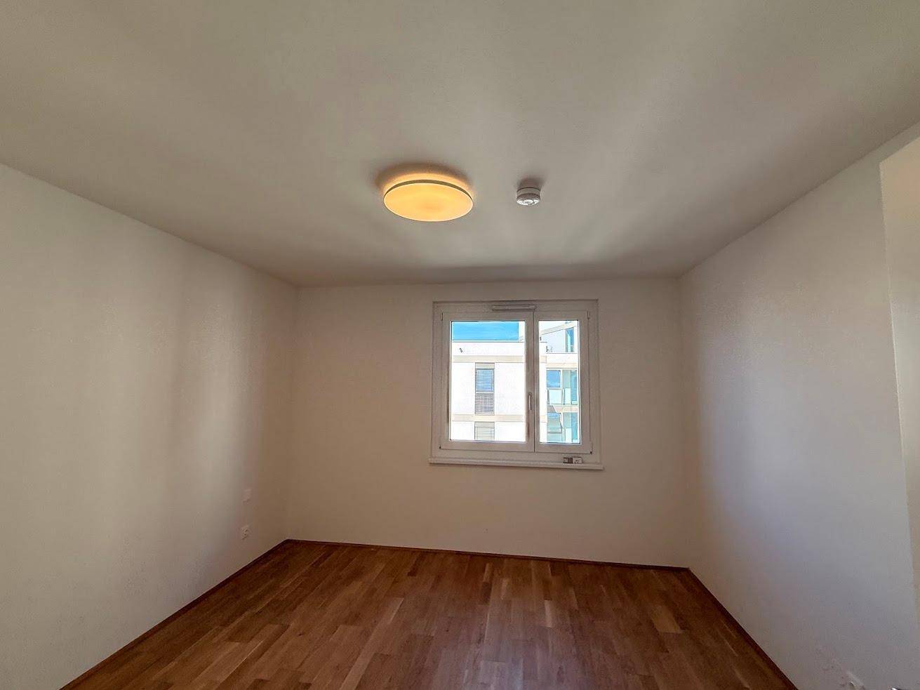 Helles Zimmer mit Parkettboden und Fenster, das viel Tageslicht hereinlässt.