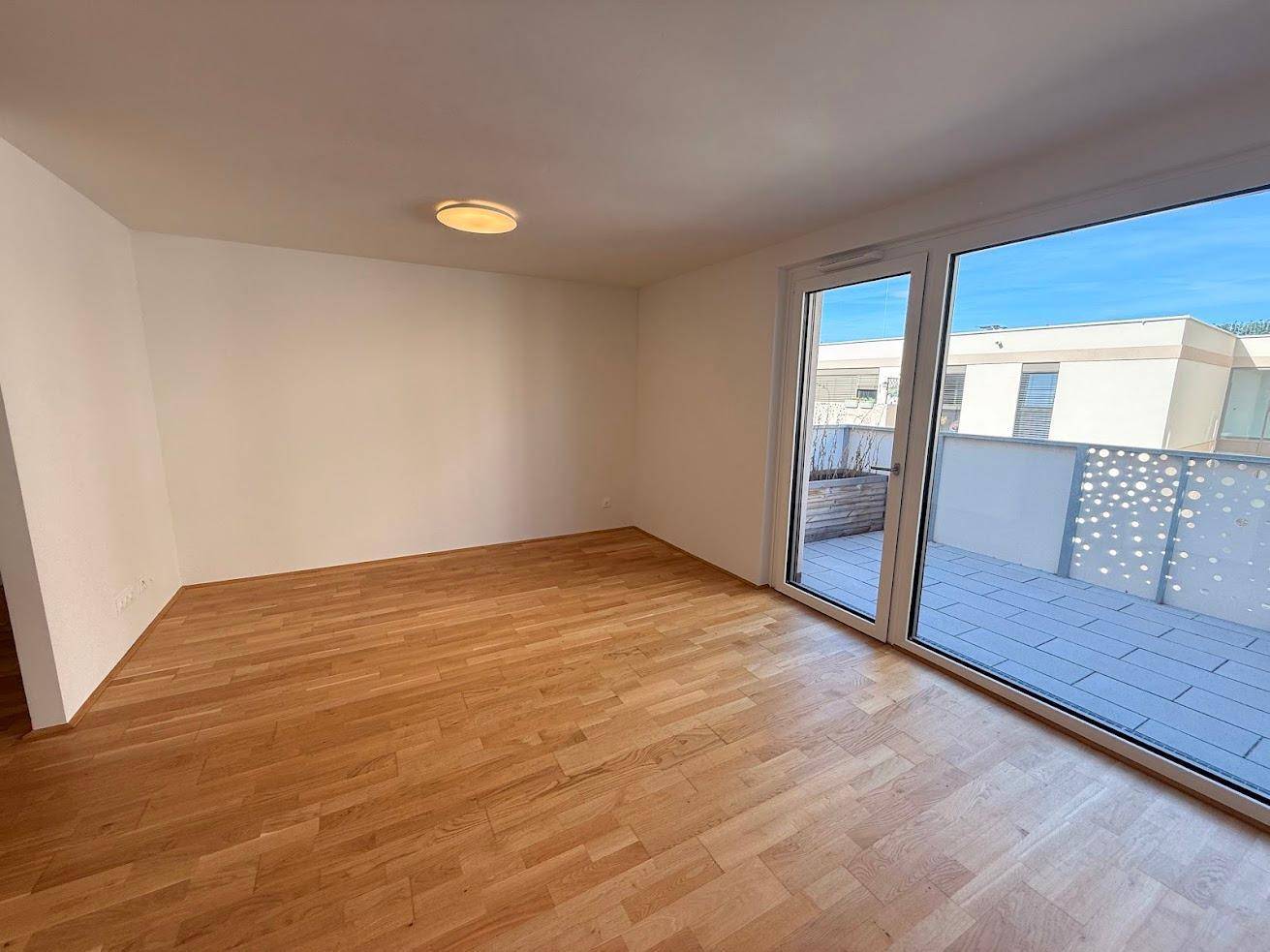 Helles Zimmer mit Parkettboden und großem Glaszugang zu einer modernen Terrasse.