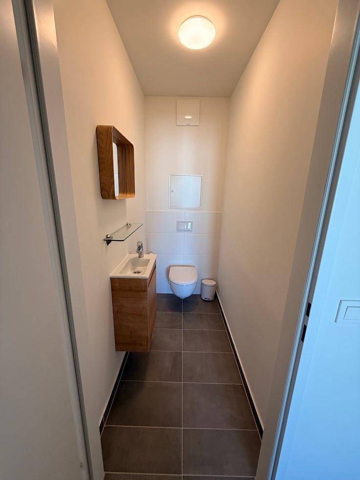 Helles Gäste-WC mit modernen Fliesen, wandhängendem WC und stilvollem Holzwaschtisch.