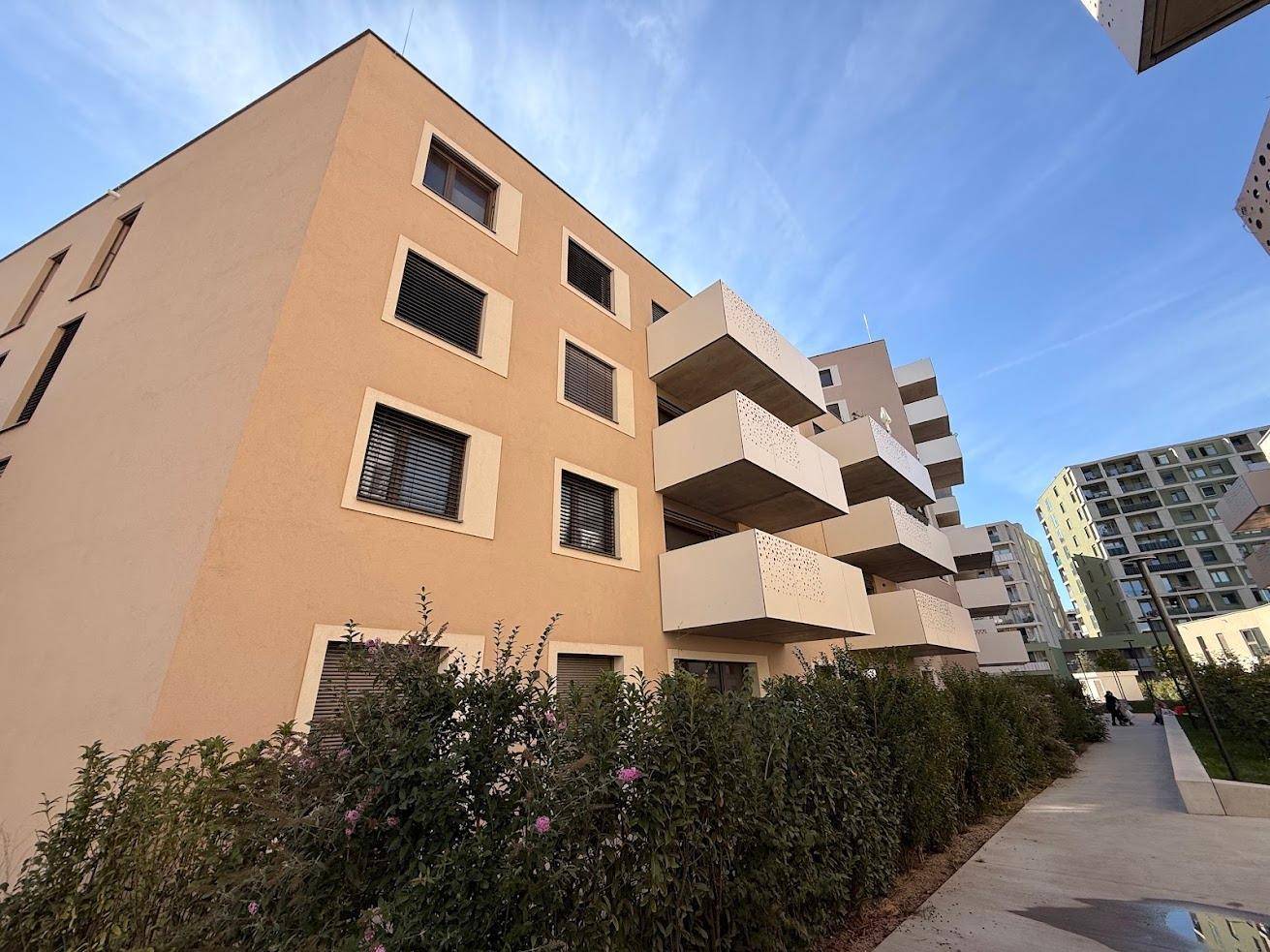 Moderne Wohngebäude-Fassade mit beige-farbenem Putz und gestuften Balkonen unter blauem Himmel.