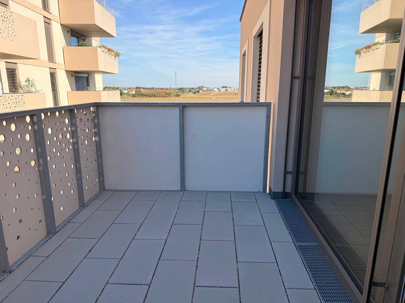 Moderner Balkon mit perforiertem Geländer und Fliesenboden, bietet einen weiten Ausblick.