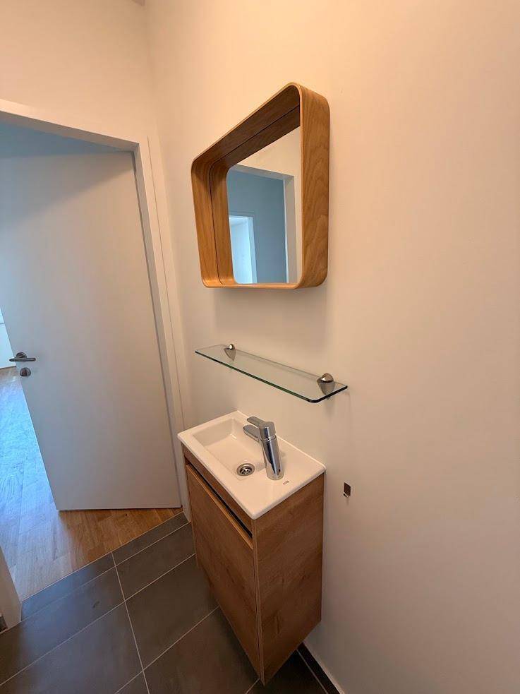 Detailansicht des Waschbereichs im Gäste-WC mit Holzunterschrank und modernem Spiegel.