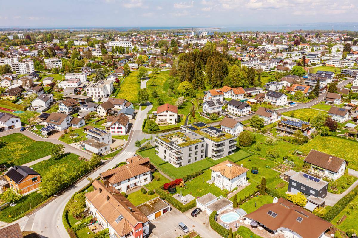 Luftaufnahme der Wohnanlage in einer grünen Umgebung mit Blick auf den Bodensee und Berge.