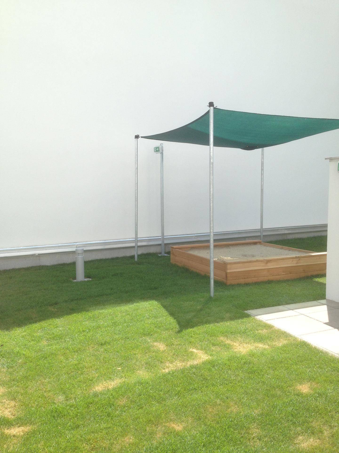 Kleiner Gartenbereich mit Rasenfläche, Sandkasten und Sonnenschutz, ideal für Kinder.