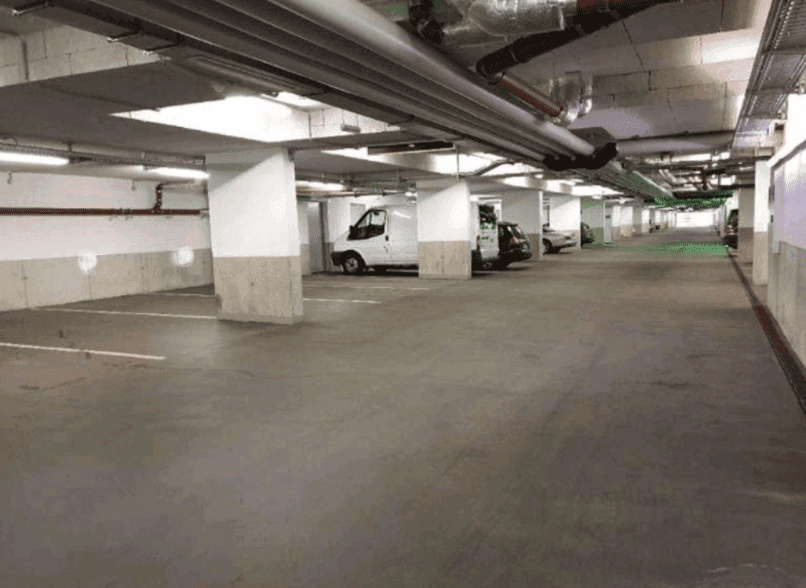 Geräumige Tiefgarage mit mehreren Stellplätzen, Betonpfeilern und sichtbaren Rohrleitungen an der Decke.