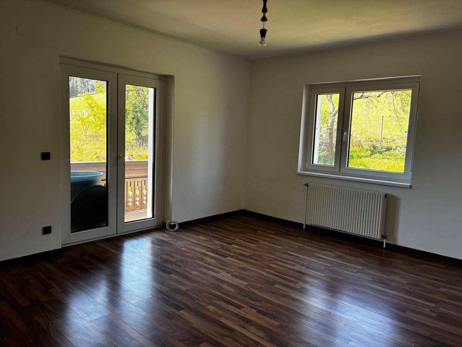 Geräumiges Zimmer mit Laminatboden, weiß gestrichenen Wänden und Zugang zu einem Balkon.