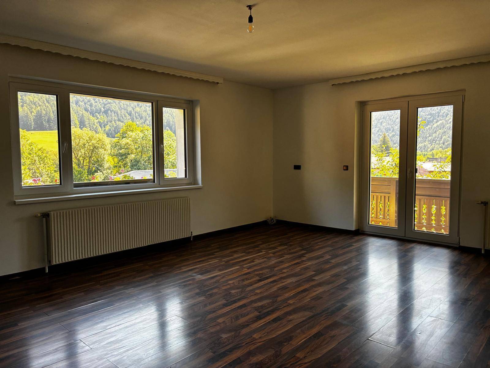 Helles Wohnzimmer mit Laminatboden, großen Fenstern und Balkonzugang mit Bergblick.