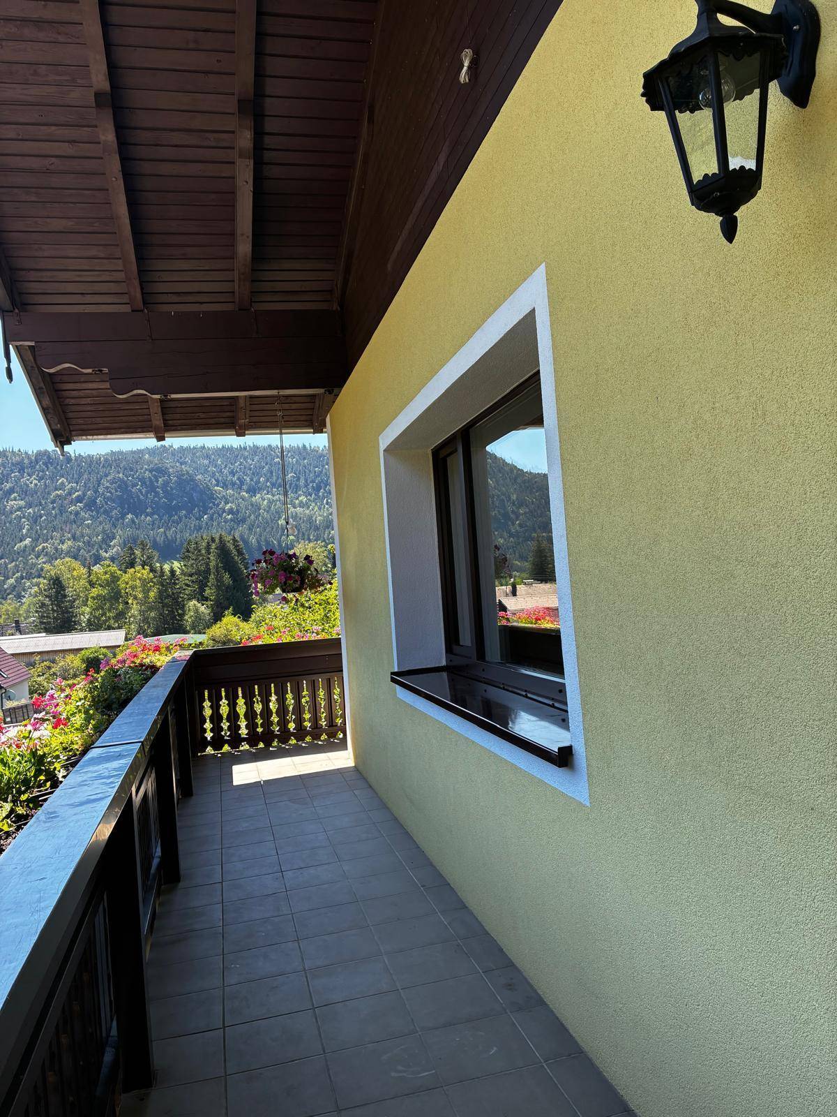 Sonniger Balkon mit Fliesenboden, Holzbalkon und weitem Blick auf die umliegende Landschaft.