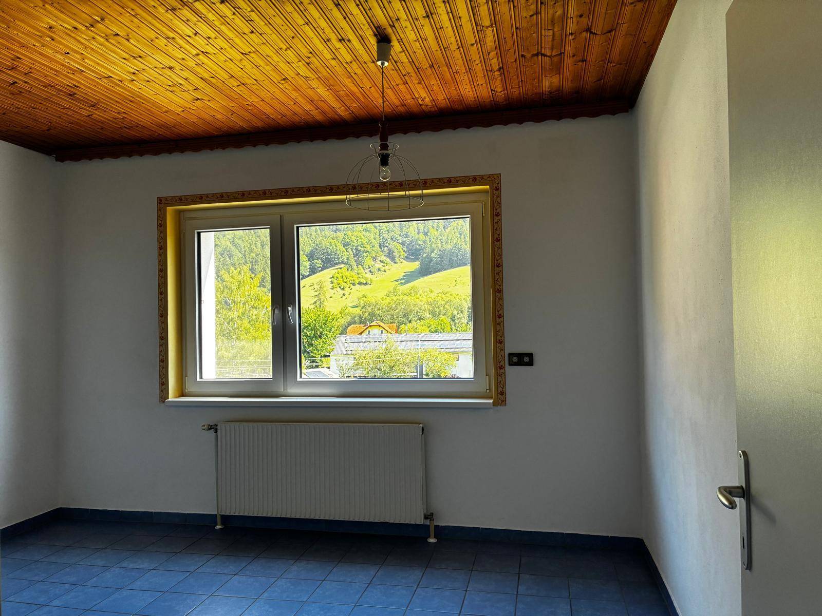 Helles Zimmer mit blauen Fliesen, weiß gestrichenen Wänden und einer Holzdecke mit Bergblick.